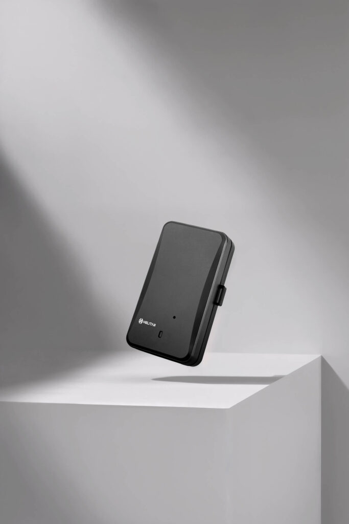 Helitar black smart GPS tracker device on minimalist gray background with soft studio lighting — modern tech product photography