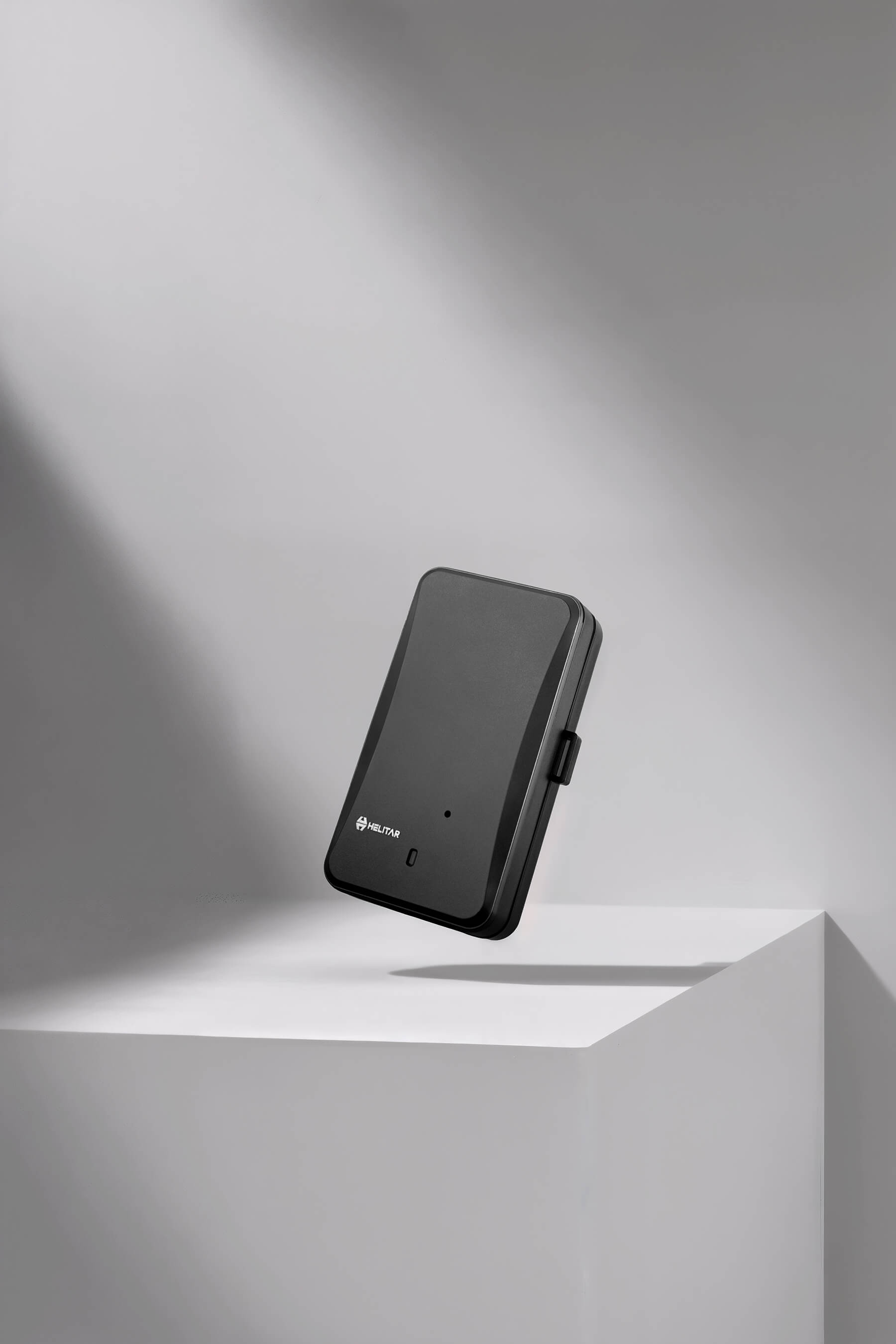 Helitar black smart GPS tracker device on minimalist gray background with soft studio lighting — modern tech product photography